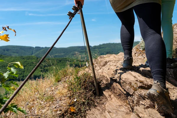 A woman walking a trail through the vineyards on a rocky, slate surface in specialized climbing shoes by a metal railing.