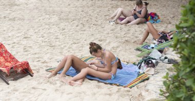 İnsanlar güneşlenmek ve kumun üzerinde bekletin. Kız bir telefon uyuşmuş çevirir