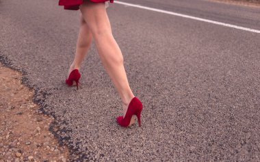 Beautiful legs of a woman wearing a short skirt and red shoes and striding down the roadway  clipart