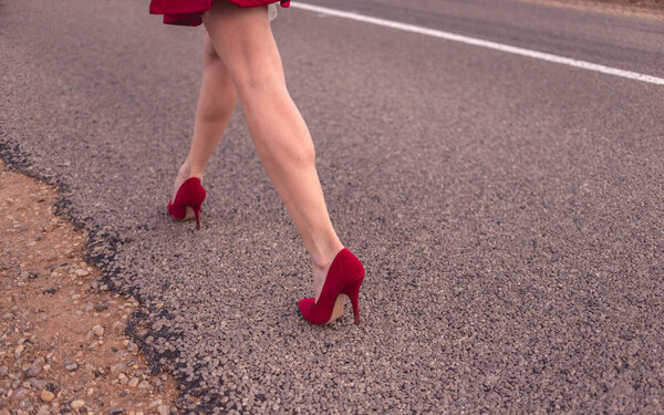 Beautiful legs of a woman wearing a short skirt and red shoes and striding down the roadway 