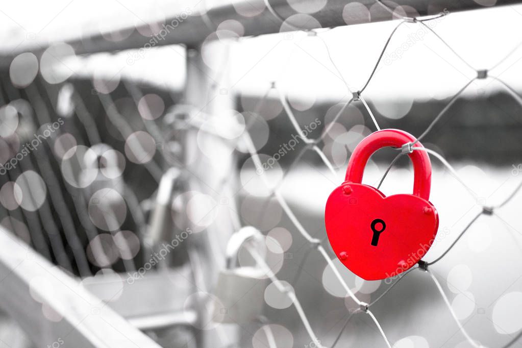 A red love padlock fastened to a bridge railing isolated on black and white background