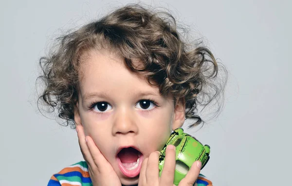 Hermoso niño rizado mirando sorprendido, chico con la boca abierta sosteniendo un juguete de coche en su mano — Foto de Stock