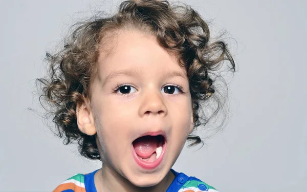 Mooie gekrulde peuter op zoek verrast, jongen met de mond open tonen zijn witte tanden — Stockfoto