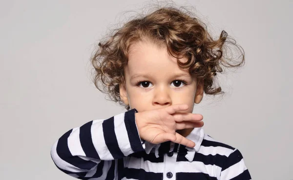 Hermoso niño rizado mirando hacia adelante y sosteniendo su mano sobre su boca, niño tratando de no hablar, cállate —  Fotos de Stock