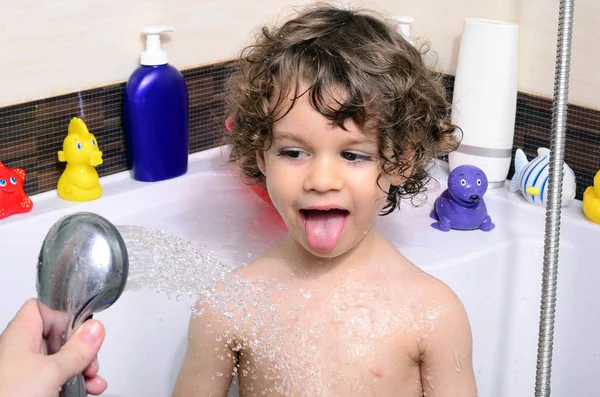 Beautiful toddler taking a bath in a bathtub with bubbles. Cute kid washing his hair with shampoo in the shower and splashing water everywhere — Stock Photo, Image