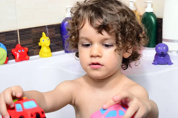 Hermoso niño tomando un baño en una bañera con burbujas. Lindo niño lavándose el cabello con champú en la ducha y salpicando agua por todas partes —  Fotos de Stock