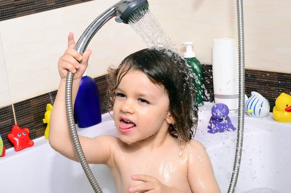 Hermoso niño tomando un baño en una bañera con burbujas. Lindo niño lavándose el cabello con champú en la ducha y salpicando agua por todas partes —  Fotos de Stock
