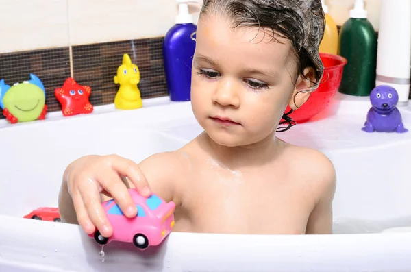 Beautiful toddler taking a bath in a bathtub with bubbles. Cute kid washing his hair with shampoo in the shower and splashing water everywhere — Stock Photo, Image