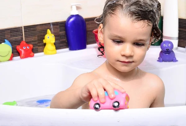 Beautiful toddler taking a bath in a bathtub with bubbles. Cute kid washing his hair with shampoo in the shower and splashing water everywhere — Stock Photo, Image