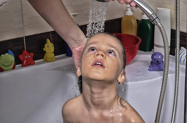 Vackra barn som badar i ett badkar med bubblor. Söta unge tvättar sitt hår med schampo i duschen och stänkande vatten överallt. Mor händer rengöring hennes smutsiga boy — Stockfoto