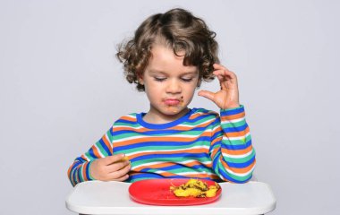 Bir çikolatalı kek yerken dağınık Başlarken çocuk. Tatlılar yemek güzel kıvırcık saçlı çocuk. Yürümeye başlayan çocuk sandalyesi aç olmak içinde.