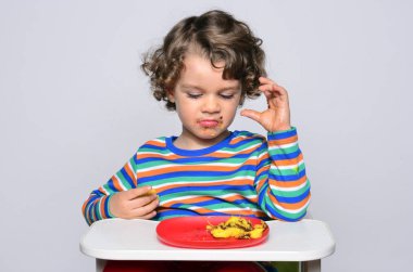 Bir çikolatalı kek yerken dağınık Başlarken çocuk. Tatlılar yemek güzel kıvırcık saçlı çocuk. Yürümeye başlayan çocuk sandalyesi aç olmak içinde.