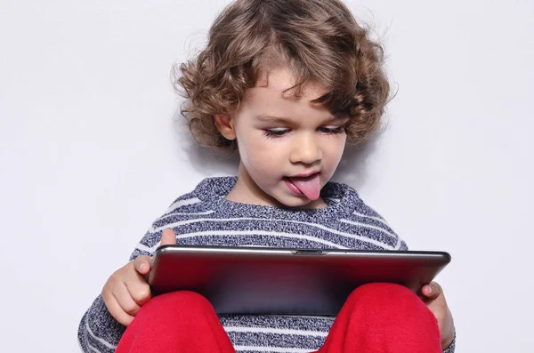 漂亮的小孩在平板电脑上玩游戏。男孩坐在地板上，看看动画片的平板显示屏上. — 图库照片