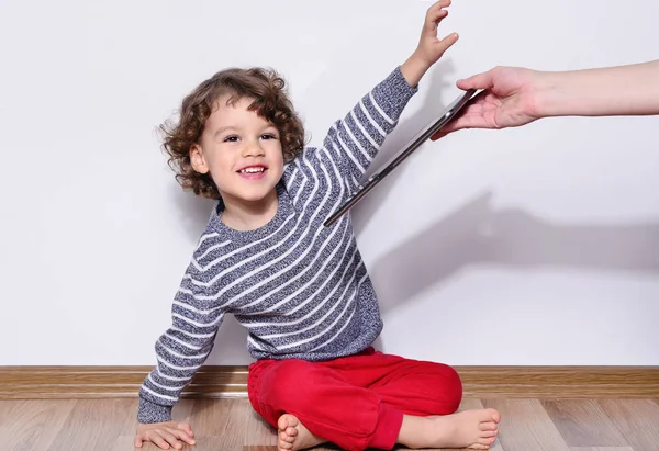 Hermoso niño jugando juegos en una tableta. Niño sentado en el suelo y mirando en la pantalla de una tableta viendo dibujos animados. Madres manos dando a su hijo una tableta y haciéndolo muy feliz — Foto de Stock