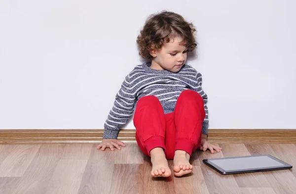 Menina bonita jogando jogos em um tablet. Menino sentado no chão e olhando para a exibição de um tablet assistindo desenhos animados . — Fotografia de Stock