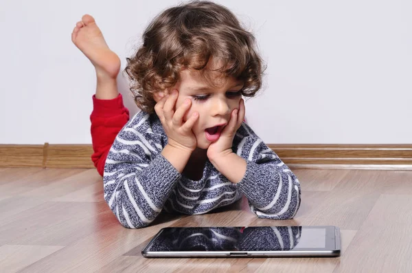 Красивый ребенок играет в игры на планшете. Мальчик сидит на полу и смотрит на дисплей планшета смотреть мультфильмы . — стоковое фото