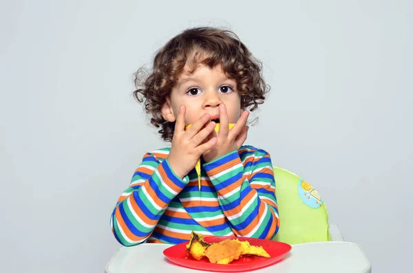 El chico se está ensuciando mientras come un pastel de chocolate. Hermoso chico de pelo rizado comiendo dulces. Niño en silla alta con hambre . —  Fotos de Stock