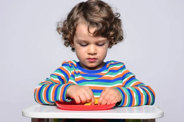 Kid getting messy while eating a chocolate cake. Beautiful curly hair boy eating sweets. Toddler in high chair being hungry. — Stock Photo, Image