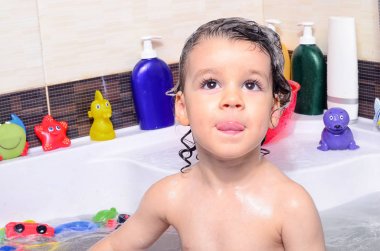Güzel yürümeye başlayan çocuk kabarcıkları ile küvette banyo. Duşta saçları şampuanla yıkama ve sıçramasına şirin çocuk her yerde su
