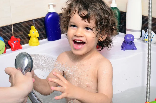 Beautiful toddler taking a bath in a bathtub with bubbles. Cute kid washing his hair with shampoo in the shower and splashing water everywhere — Stock Photo, Image