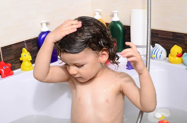 Beautiful toddler taking a bath in a bathtub with bubbles. Cute kid washing his hair with shampoo in the shower and splashing water everywhere — Stock Photo, Image