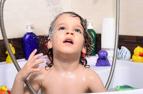 Vackra barn som badar i ett badkar med bubblor. Söta unge tvättar sitt hår med schampo i duschen och stänkande vatten överallt — Stockfoto