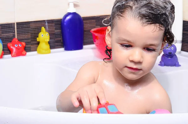 Beautiful toddler taking a bath in a bathtub with bubbles. Cute kid washing his hair with shampoo in the shower and splashing water everywhere — Stock Photo, Image