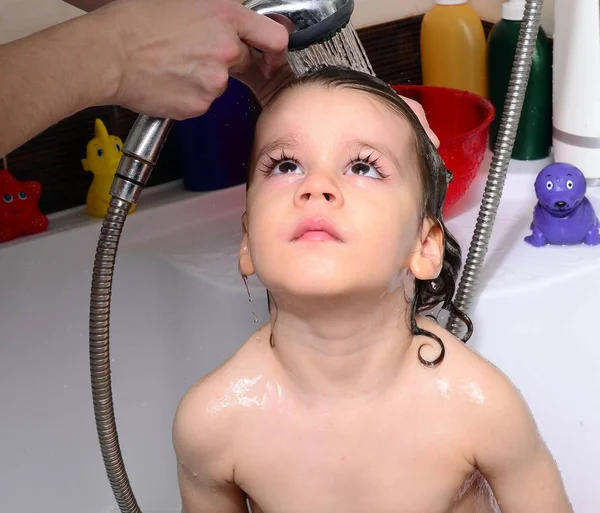 Beautiful toddler taking a bath in a bathtub with bubbles. Cute kid washing his hair with shampoo in the shower and splashing water everywhere — Stock Photo, Image