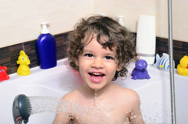 Bellissimo bambino che fa il bagno in una vasca da bagno con bolle. Bambino carino lavarsi i capelli con shampoo sotto la doccia e spruzzare acqua ovunque Immagini Stock Royalty Free