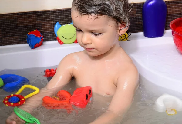 Hermoso niño tomando un baño en una bañera con burbujas. Lindo niño lavándose el cabello con champú en la ducha y salpicando agua por todas partes Imagen De Stock