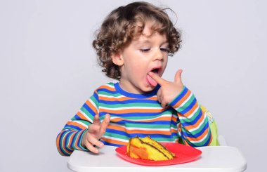 Bir çikolatalı kek yerken dağınık Başlarken çocuk. Tatlılar yemek güzel kıvırcık saçlı çocuk. Yürümeye başlayan çocuk sandalyesi ağzını pasta ile doldurma aç olmak içinde 
