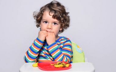Bir çikolatalı kek yerken dağınık Başlarken çocuk. Tatlılar yemek güzel kıvırcık saçlı çocuk. Yürümeye başlayan çocuk sandalyesi ağzını pasta ile doldurma aç olmak içinde 