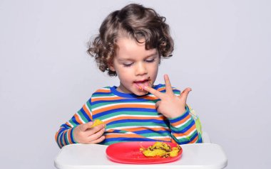 Bir çikolatalı kek yerken dağınık Başlarken çocuk. Tatlılar yemek güzel kıvırcık saçlı çocuk. Yürümeye başlayan çocuk sandalyesi ağzını pasta ile doldurma aç olmak içinde 