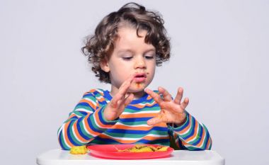 Bir çikolatalı kek yerken dağınık Başlarken çocuk. Tatlılar yemek güzel kıvırcık saçlı çocuk. Yürümeye başlayan çocuk sandalyesi ağzını pasta ile doldurma aç olmak içinde 