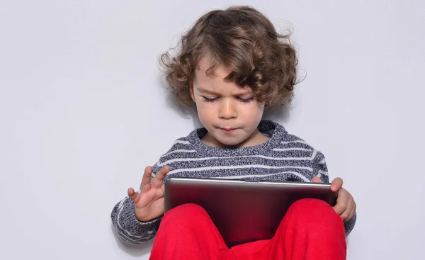 Menina bonita jogando jogos em um tablet. Menino sentado no chão e olhando para a tela, scteen de um tablet assistindo desenhos animados . — Fotografia de Stock