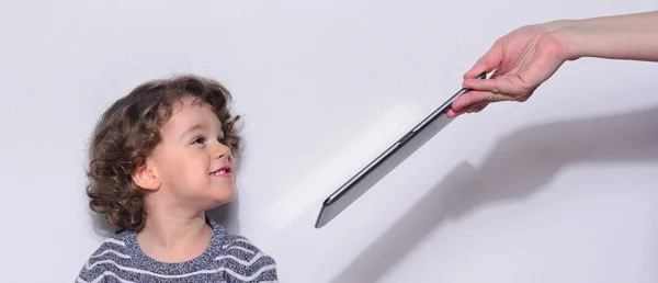 Hermoso niño jugando juegos en una tableta. Niño sentado en el suelo y mirando en la pantalla de una tableta viendo dibujos animados. Chico muy feliz porque su madre le quitó la tableta —  Fotos de Stock