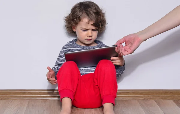 漂亮的小孩在平板电脑上玩游戏。男孩坐在地板上，看看动画片的一款平板电脑的显示屏上。非常生气因为他的母亲给他了这款平板电脑的孩子 — 图库照片