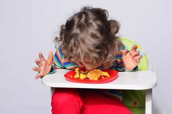 Kid getting messy while eating a chocolate cake. Beautiful curly hair boy eating sweets. Toddler in high chair being hungry stuffing his mouth with cake — Stock Photo, Image