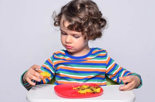 Kid getting messy while eating a chocolate cake. Beautiful curly hair boy eating sweets. Toddler in high chair being hungry stuffing his mouth with cake — Stock Photo, Image