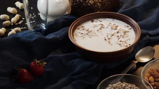 Strawberries fall in muesli with milk in a clay plate on a dark blue towel — Stock Video