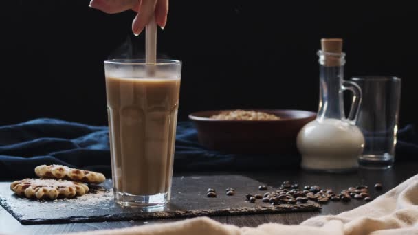 Café com leite é mexido com uma colher em um vidro transparente, vídeo em câmera lenta vista lateral — Vídeo de Stock