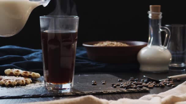 Γάλα χύνεται από μια καράφα σε ένα καθαρό ποτήρι καφέ, σκούρο φόντο, βίντεο αργής κίνησης — Αρχείο Βίντεο