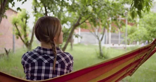 Flickan sitter tillbaka i ramen, svingande på en hängmatta Stockvideo