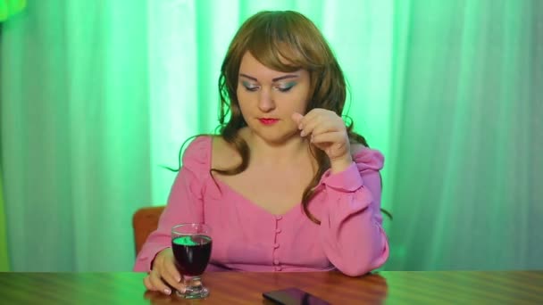 Kızıl saçlı genç kadın telefona bakar ve elinde bir bardak kırmızı şarap tutar.. — Stok video