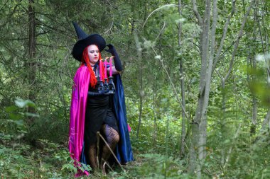 Elinde yanan bir mumla ormanda şapkalı bir büyücü ve ormanda mor bir pelerin var..