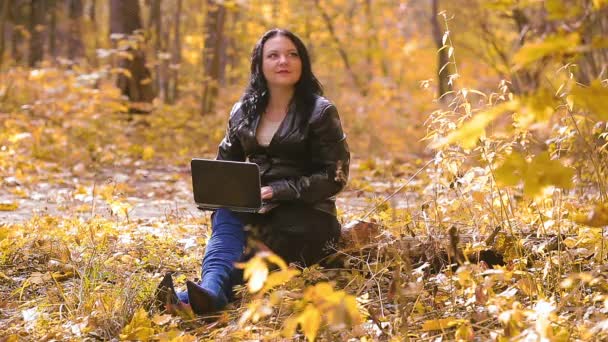 Uma jovem judia de botas azuis senta-se em um parque em um dia ensolarado de outono e trabalha remotamente com um laptop — Vídeo de Stock