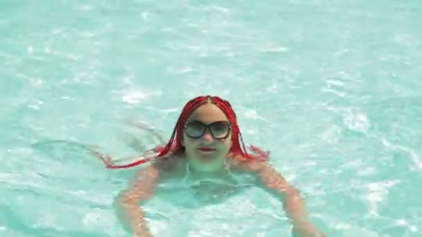 Eine junge Frau im weißen Badeanzug schwimmt im Pool. — Stockvideo