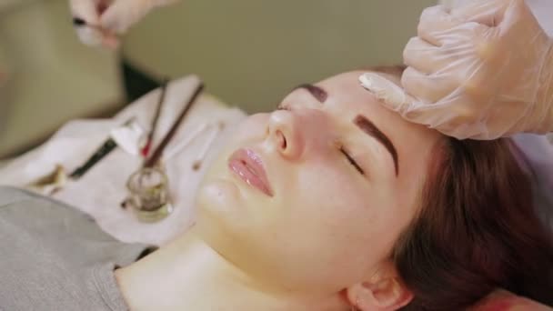Die Kosmetikerin wäscht der Kundin Henna von den Augenbrauen und trägt eine spezielle Creme auf. — Stockvideo