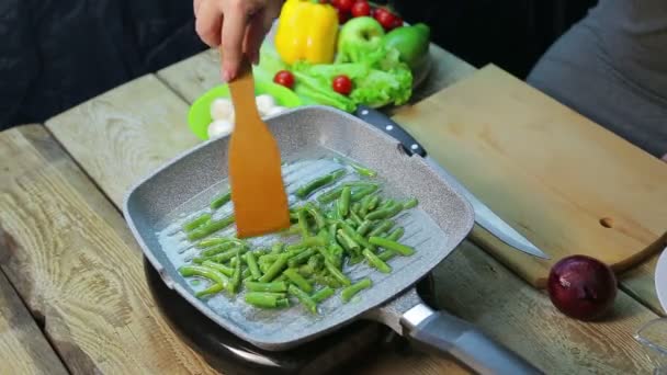 Weibliche Hand mit einem Holzspatel rührt grüne Bohnen in Öl gebraten in einem pa — Stockvideo