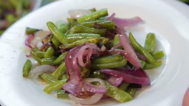 Samičí ruka rozprostírá smažené zelené fazole s cibulí v bílém talíři — Stock video